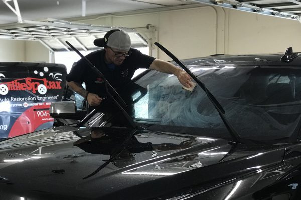 A man is working on the windshield of his car.