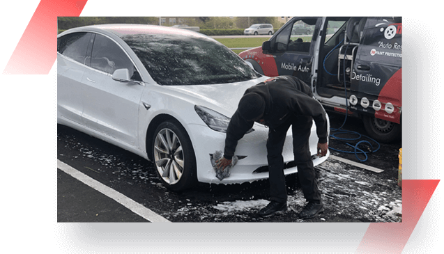 A man washing his white car in the street.